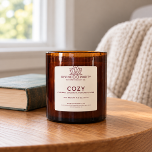 Divine Purity Cozy candle beside a book and soft knit blanket